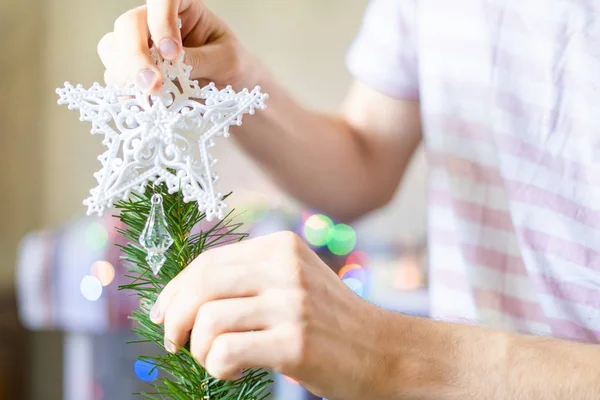 close up person\'s hands putting white decoration star on top of christmass tree f