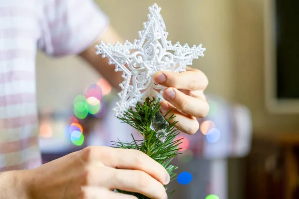 close up person\'s hands putting white decoration star on top of christmass tree f