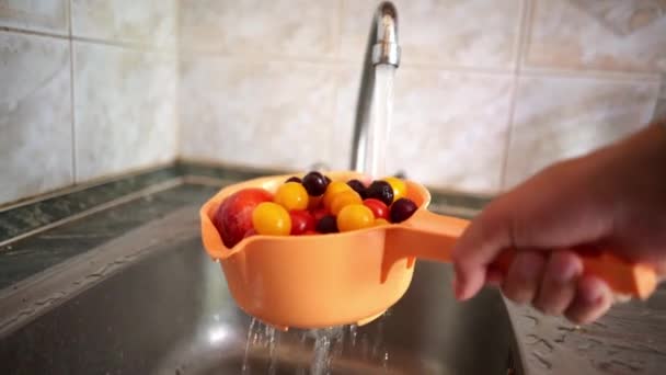 Рука тримає друшляк зі свіжими фруктами та ягодами і миє його на кухні з водою — стокове відео
