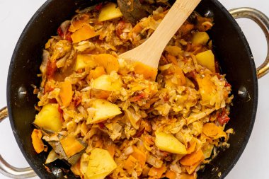 Renkli bir yüzey üzerinde ahşap sopayla sebze güveci karışımının üst görünümü