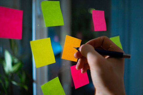 person taking down some notes on a color sticker on the window glass