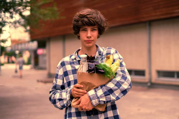 young man going home from the grocery store with fresh fruit and vegetables in the paper bag