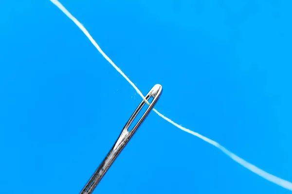 Tiro macro de um olho de agulha com um fio que passa por ele em fundos a cores — Fotografia de Stock