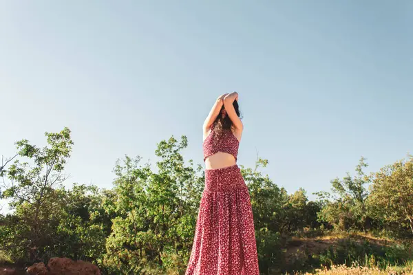 青い空に対して長い夏のドレスで腕で顔を覆う女性 — ストック写真