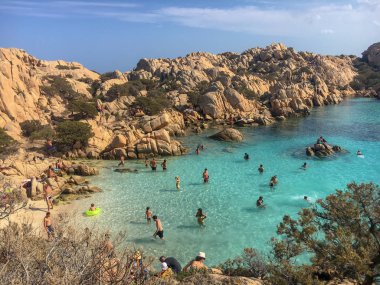 Caprera, İtalya - 8 Eylül 2017: Beach life Spiaggia Cala Coticcio taşlara Caprera İtalyan Adası üzerinde oturan kişi ile