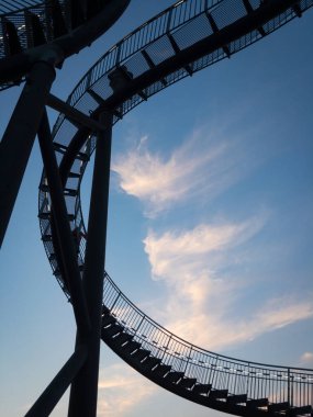 Duisburg, Almanya 28 Ağustos 2018: Yürünebilir Tiger & Turtle roller coaster heykeli gökyüzüne karşı Magic Mountain 'da. İnşaat, basamakları ve endüstri kültürünün bir parçası olan aydınlatılmış bir iskele..