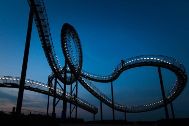 Duisburg, Almanya 28 Ağustos 2018: Yürüyebilen Kaplan ve Kaplumbağa roller coaster heykeli geceleyin Sihirli Dağ 'da. İnşaat, basamakları ve endüstri kültürünün bir parçası olan aydınlatılmış bir iskele..
