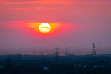 Bulutlarla ve yüksek voltajlı elektrik hattıyla güneş batıyor.