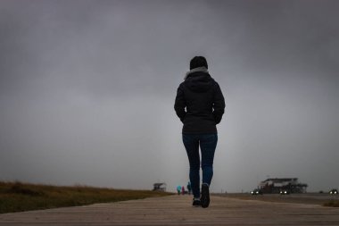 Kuzey sahilinde gökyüzüne karşı tahta bir patikada yürüyen tanınmayan bir kadının alçak açılı görüntüsü.