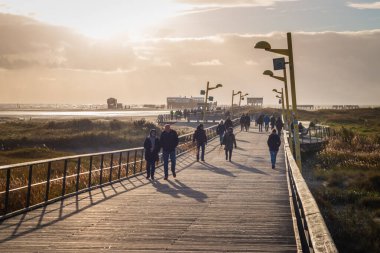 Sankt Peter-Ording, Almanya 4 Ekim 2018: Güneşli bir sonbaharda güneşli bir günde gökyüzüne karşı ahşap kanalizasyonda yürüyen insanlar.