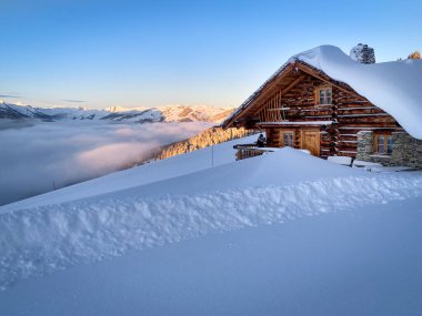 Avusturya Alpleri 'ndeki Saalbach Hinterglemm kayak bölgesindeki eski çiftlik evi, gün doğumunda mavi gökyüzüne karşı karla kaplıydı.