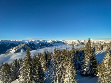 Avusturya 'da Saalbach Hinterglemm kayak bölgesinde kar manzaralı dağlar sabah mavi gökyüzüne karşı bulutlardan oluşan bir battaniyenin altında