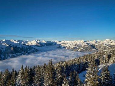 Avusturya 'da Saalbach Hinterglemm kayak bölgesinde kar manzaralı dağlar sabah mavi gökyüzüne karşı bulutlardan oluşan bir battaniyenin altında