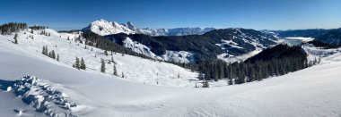 Avusturya 'daki Saalbach Hinterglemm kayak bölgesindeki karlı dağların panoramik manzarası mavi gökyüzüne karşı.