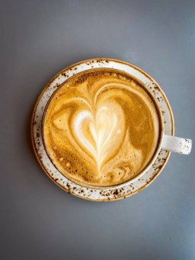 İzlanda 'da rahat bir kafede gri bir masada kalp şeklinde latte sanatıyla kapuçinonun yakın çekimi.