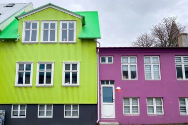 Reykjavik, İzlanda 'da bulutlu gökyüzüne karşı yeşil çatılı ve beyaz pencereli parlak pembe ve ıhlamur yeşili binalar