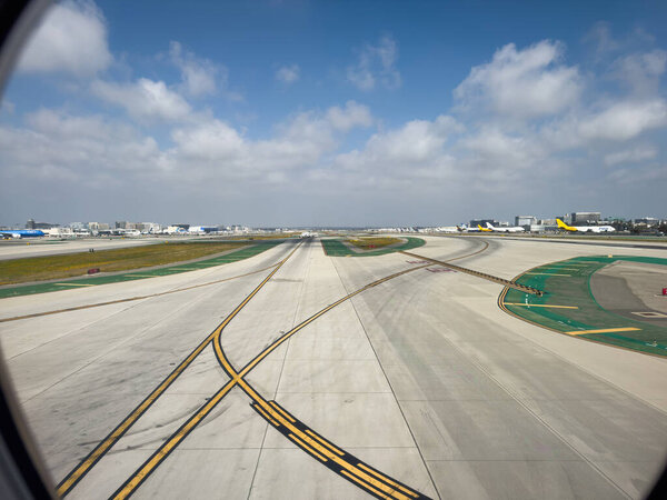 Los Angeles, California, USA - April 19, 2024: View of runways and taxiways at International Airport LAX with aircrafts and airport buildings against partially cloudy sky seen through the airplane window