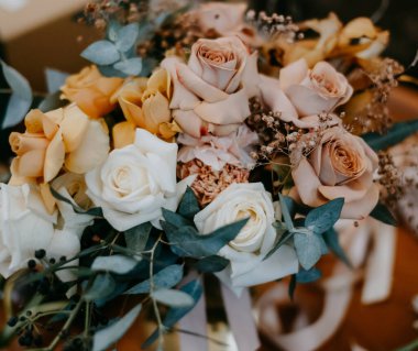 Gelinin düğün buketi beyaz, sarı, pembe güller masada duruyor.