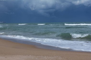 Kumlu kumsalın üzerindeki mavi fırtına bulutları koyu mavi suyla kaplı.