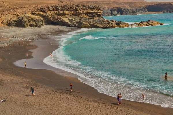 位于西班牙加那利群岛弗尔特文图拉的壮观的黑色沙滩和背景为海湾的山脉 人们在海岸上沐浴和日光浴 — 图库照片