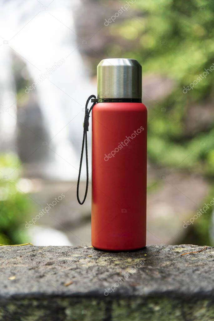 Red thermal bottle over rocky surface with waterfall on the back on the Atlantic Rainforest in Tijuca Forest Park, Rio de Janeiro, Brazil