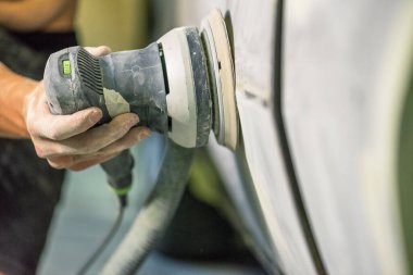 Araba tamirhanesinde araba cilalayan bir adamın elinde öğütücü..