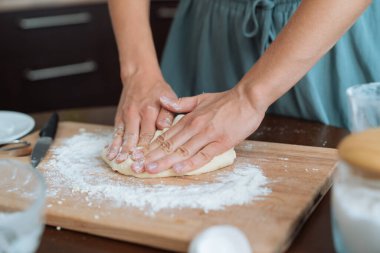 Kadının elleri evde hamur yoğuruyor.