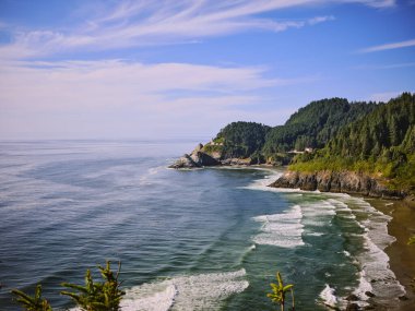 Oregon sahilinde deniz feneri olan ormanlık bir sahil koyunda..