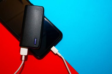 Powerbank mavi ve kırmızı arka planda bir cep telefonu yüklüyor. Powerbank konsepti.