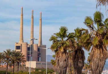 Şehrin ortasında fabrikalar, palmiye ağaçları ve duvar yazıları.