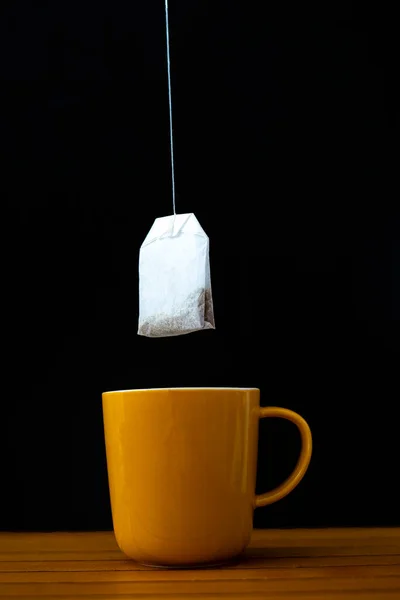 Putting a tea bag in a yellow cup. Tea concept.