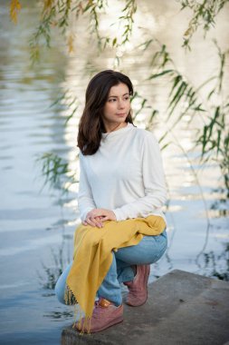 Güzel esmer kız sonbaharda nehir kenarında poz veriyor. 