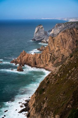 Denizin üzerindeki günbatımının ve dalgaların aydınlattığı doğal bir uçurum manzarası.