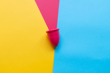 Renkli arka planda pembe adet bardağı, kadın mahrem hijyen dönemi ürünleri, üst görünüm, düz yatak, metin için kopyalama alanı.