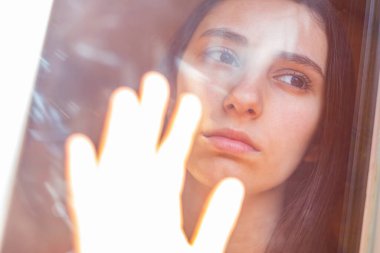 Pencereden dışarı bakan bir kadın. Karantina ve COVID-19 kavramı. Pencereye elle dokunmak.