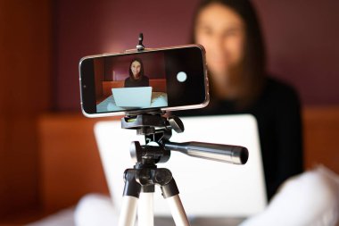 Cep telefonu tripodda, evde bir kadın vlogger kaydediyor. Vlog yazarı kavramı.