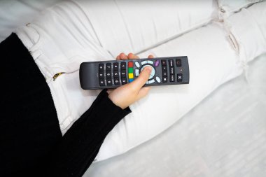 Yatakta uzaktan kumanda kullanan bir kadın. Uzaktan kumandalı televizyon kavramı.