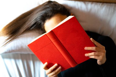 young woman covered her face with red book while reading