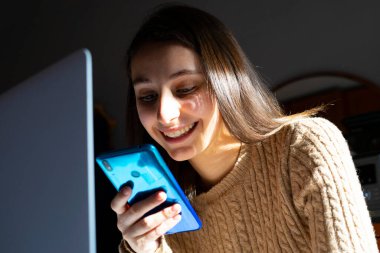 Cep telefonuna ve bilgisayarına bakan bir kadın. Ev konseptinde çalış.