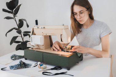 Gribi önlemek için evdeki dikiş makinesine koruyucu ilaç maskesi takan bir kız. Covid-19 beyaz arka plan ev işyeri olan odada.