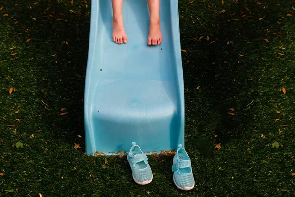 地面に靴を履いた青いスライド上の裸足の子供 — ストック写真