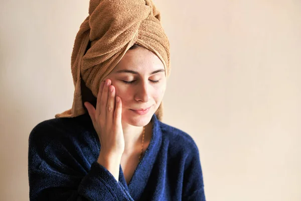 woman in a robe and with a towel on her head applies cosmetics to skin