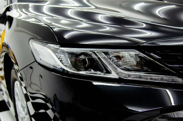 Car details - luxurious modern headlights and shiny black car bonnet