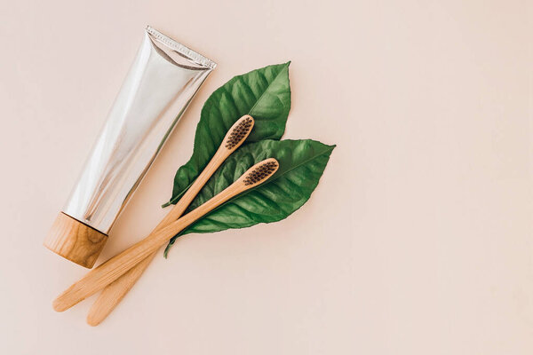 Бамбуковые натуральные зубные щетки, зубная паста и свежие листья на бледном фоне. Концепция без отходов и пластика. Концепция устойчивого образа жизни.