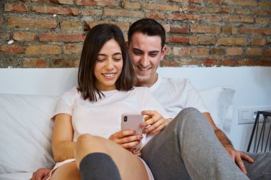 Evde yatarken cep telefonuna bakan genç bir çift.