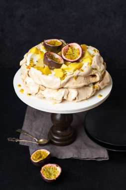 Tutku meyveli Pavlova keki, mango, limon ve muz kreması koyu arkaplanda.