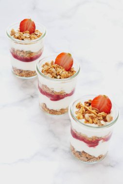 Yoğurt-çilek reçeli ve taze çilekli küçük kavanozlar dolusu granola. Sağlıklı vejetaryen kahvaltı konsepti. Ortasına odaklan..
