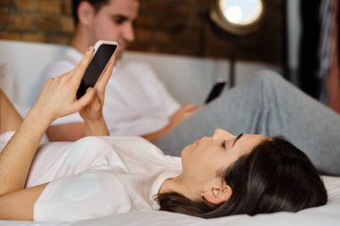 Evde yatarken cep telefonuna bakan genç bir kadın.