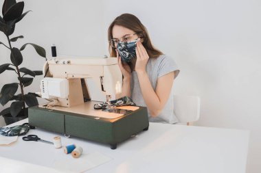 Gribi önlemek için evdeki dikiş makinesine koruyucu ilaç maskesi takan bir kız. Covid-19 beyaz arka plan ev işyeri olan odada.