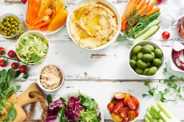 Humus sosu ve çiğ vejetaryen atıştırmalıkları beyaz ahşap masada. Boşluğu kopyala                             